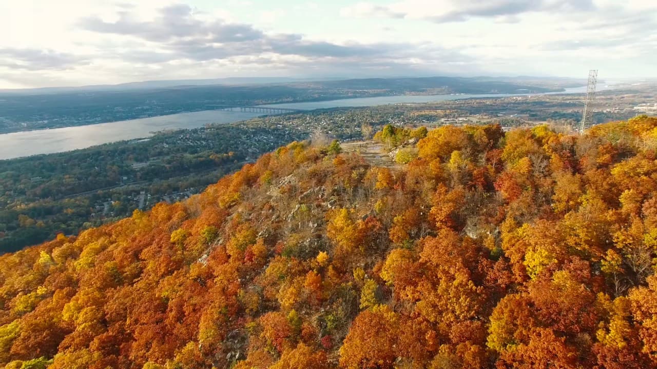 Aerial view of a hillside covered in vibrant autumn foliage overlooking a river.