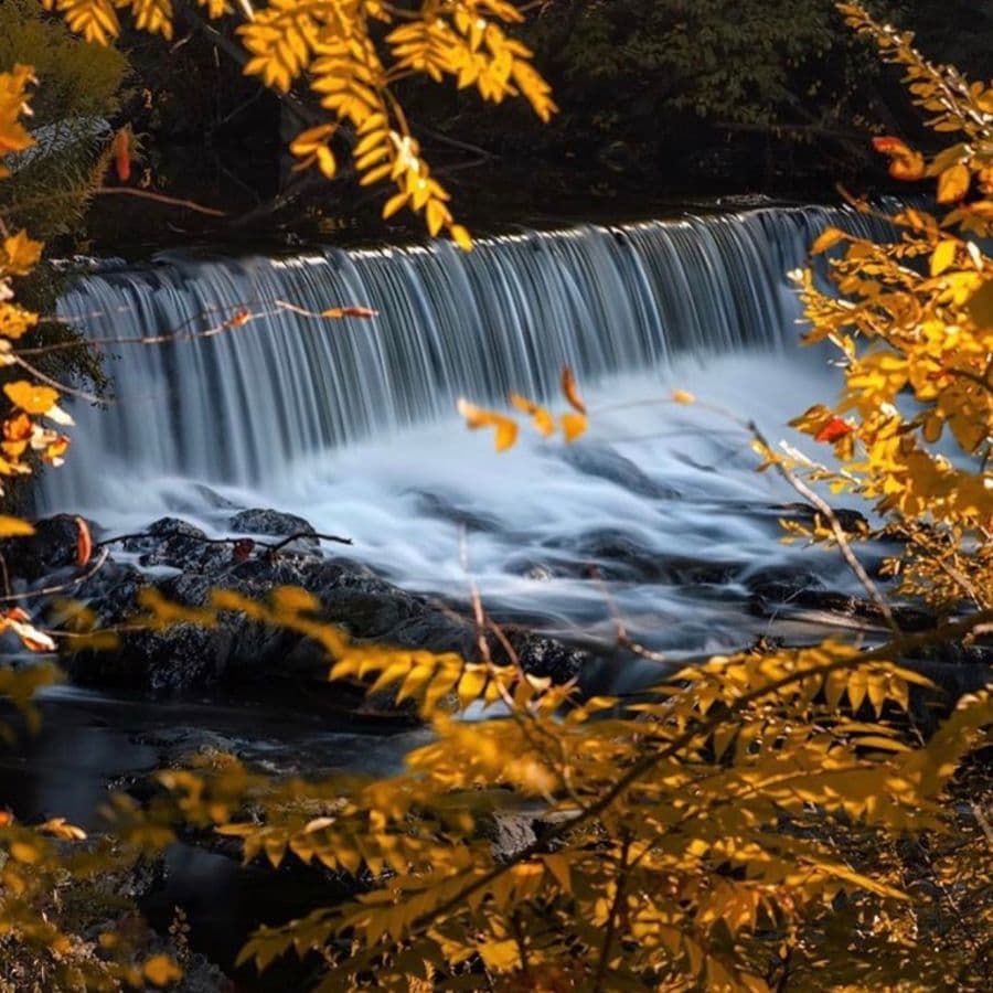 A serene waterfall cascades over rocks, framed by vibrant autumn leaves.